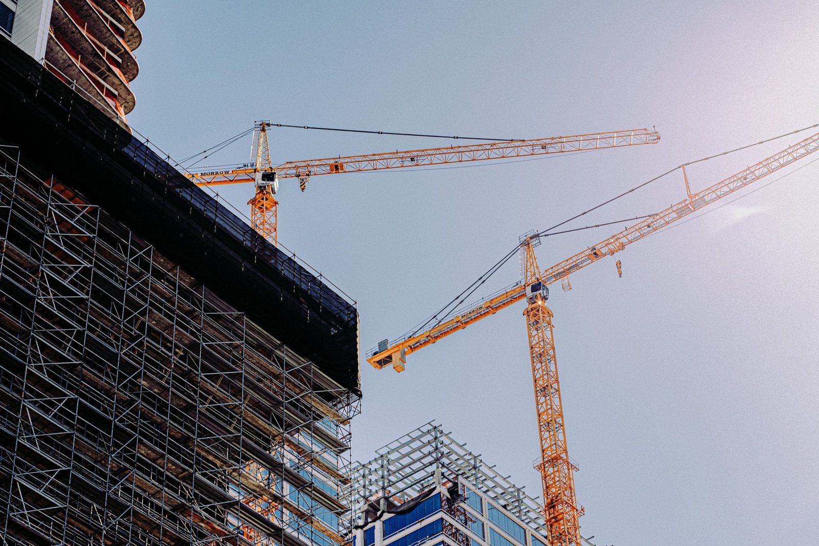 Tower cranes beside a building rising behind scaffolding